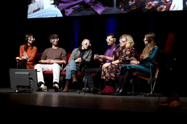 Talk-Runde mit Gäst*innen auf der Bühne. Alle tragen alte 3D-Brillen